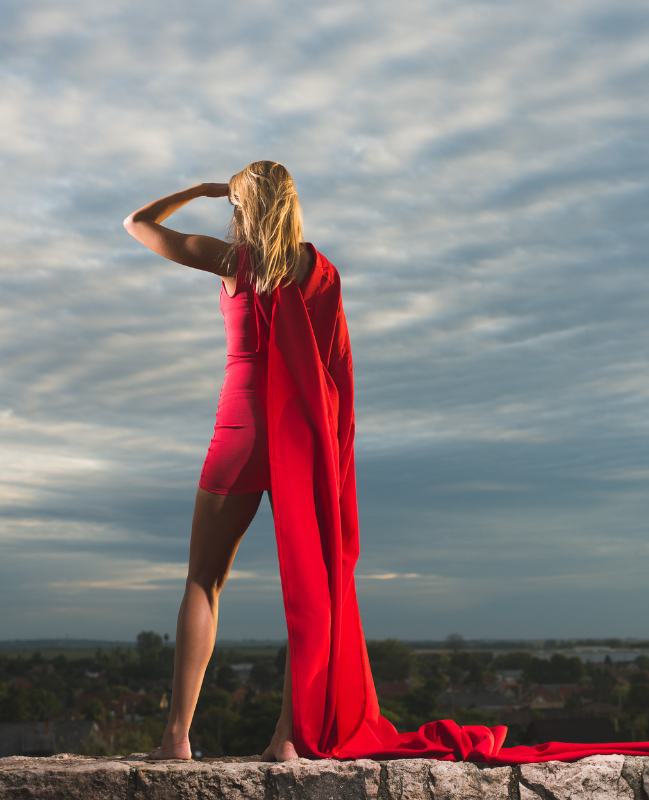 Back of a woman wearing a long red cape looking up at the sky.