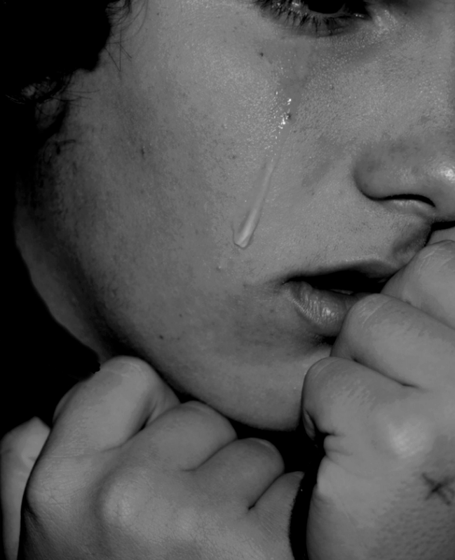 B&W photo of a woman with her hands held to her chin and mouth and a tear falling from her eye