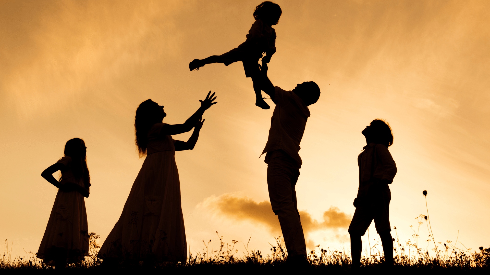 A silhouette of a family, under a bright sky, with the man holding a child high and the woman reaching ups and the other children looking up